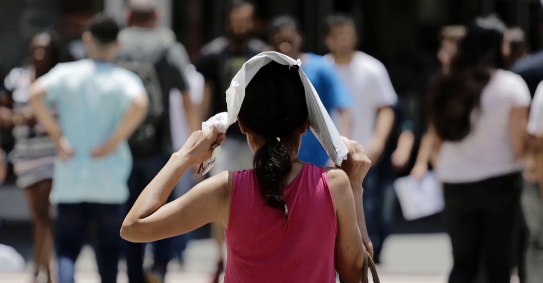 Una mujer se protege del sol caliente mientras camina en una calle del centro durante una ola de calor extrema