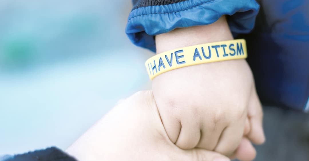 Imagen de autismo: pulsera en la muñeca de un niño con el mensaje: tengo autismo -mamá sujeta a su hijo autista